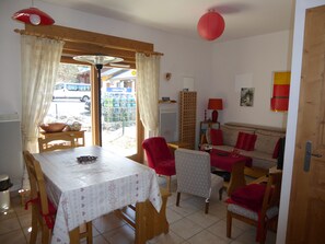 Ein Essbereich mit Tisch und Stühlen, einer Couch, einer roten Lampe und Blick ins Freie.