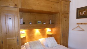A wooden room with a bed, shelves with books and decorative items, and a wall-mounted light fixture. - Pleasant 3-room apartment with garden, close to the center (Pralognan-la-Vanoise)