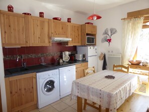 A compact kitchen with wooden cabinets, a washing machine, a microwave, and a dining area with a table.