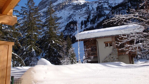 A wooden cabin with a snow-covered roof, surrounded by snow-covered trees and mountains in the background. - Pleasant 3-room apartment with garden, close to the center (Pralognan-la-Vanoise)