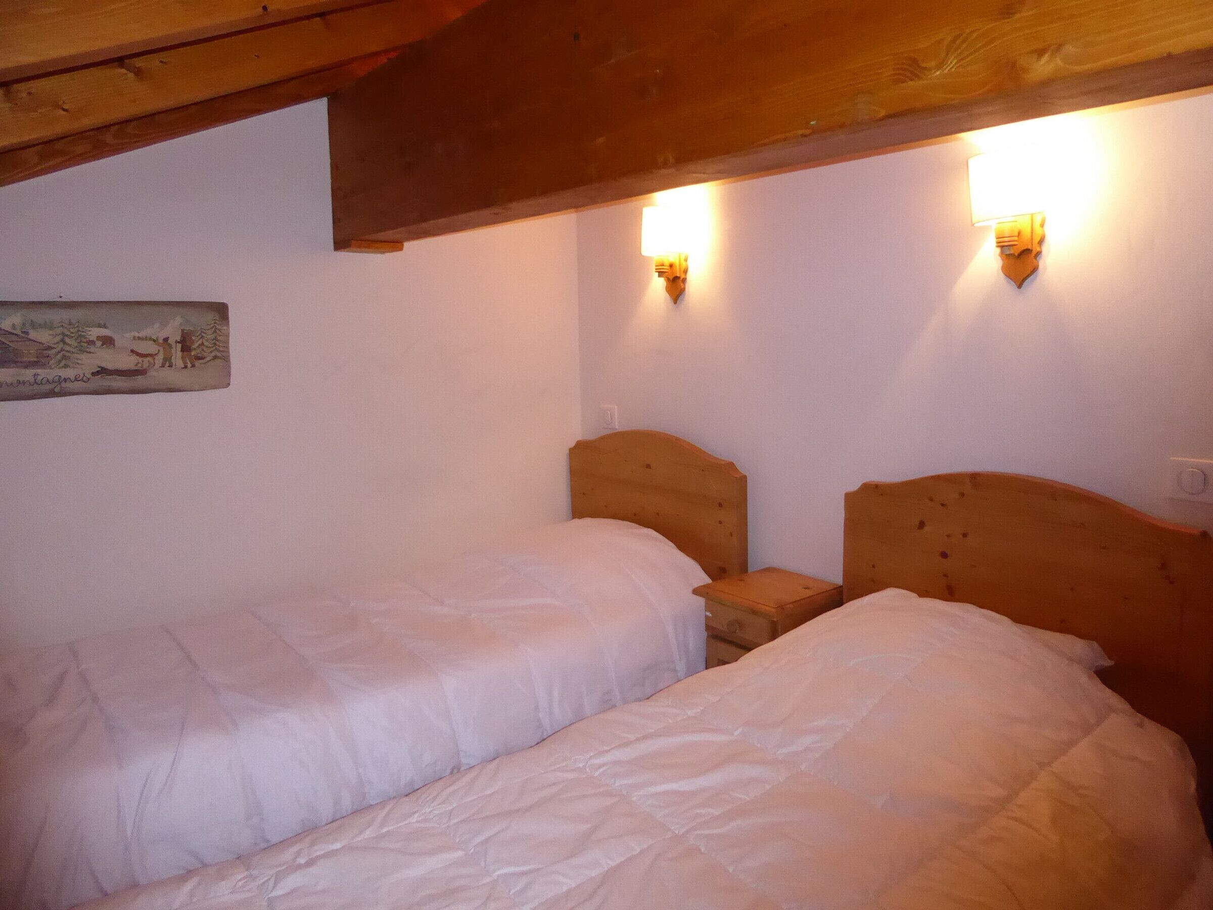 A bedroom with two wooden beds, a wooden ceiling, and wall-mounted lights.