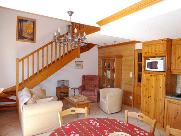 Ein gemütliches Wohnzimmer mit einer Holztreppe, einer Kandelaber und einem Tisch mit roter Tischdecke, sowie eine Küchenzeile mit Holdekor und einer Mikrowelle.