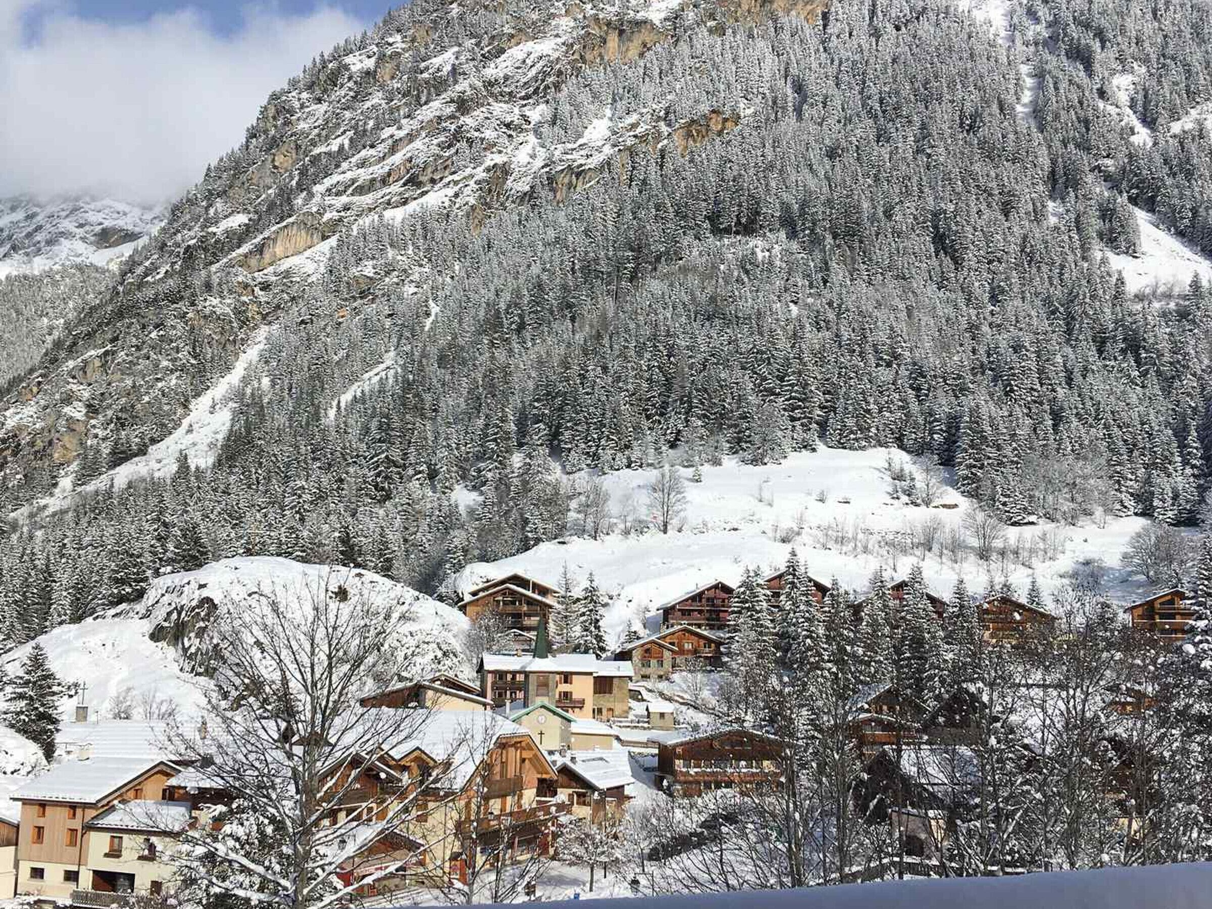 Une montagne enneigée, sur laquelle se dressent plusieurs chalets en bois.