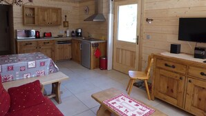 Een knus, chalet-achtig vertrek met houten wanden, een kitchenette, een eethoek met tafel en stoelen, en een televisie.