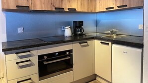 A compact kitchen with wooden cabinets, a built-in oven, a coffee maker, and a sink. - Cozy studio near slopes, quiet with closed garage (Pralognan-la-Vanoise)