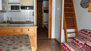 A compact kitchen with a microwave, stove, and sink. A wooden ladder is next to a bed with a patterned blanket. - Cozy studio near slopes, quiet with closed garage (Pralognan-la-Vanoise)