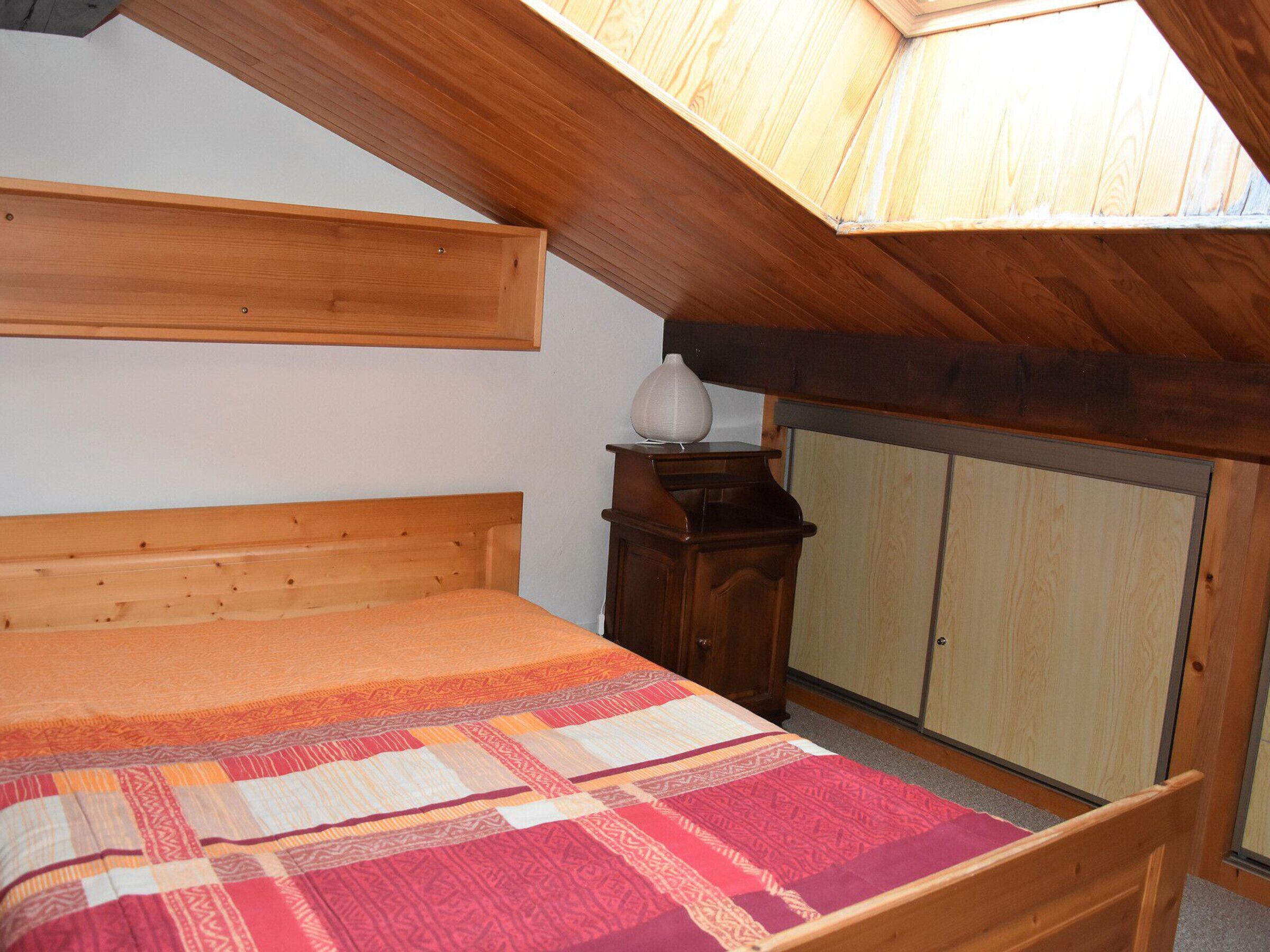Een slaapkamer met een houten bed, nachtkastje, kledingkast en dakraam.