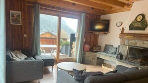 Ein Wohnzimmer mit einer Couch, einem Fernseher, einem Kamin und Blick durch eine Glastür.