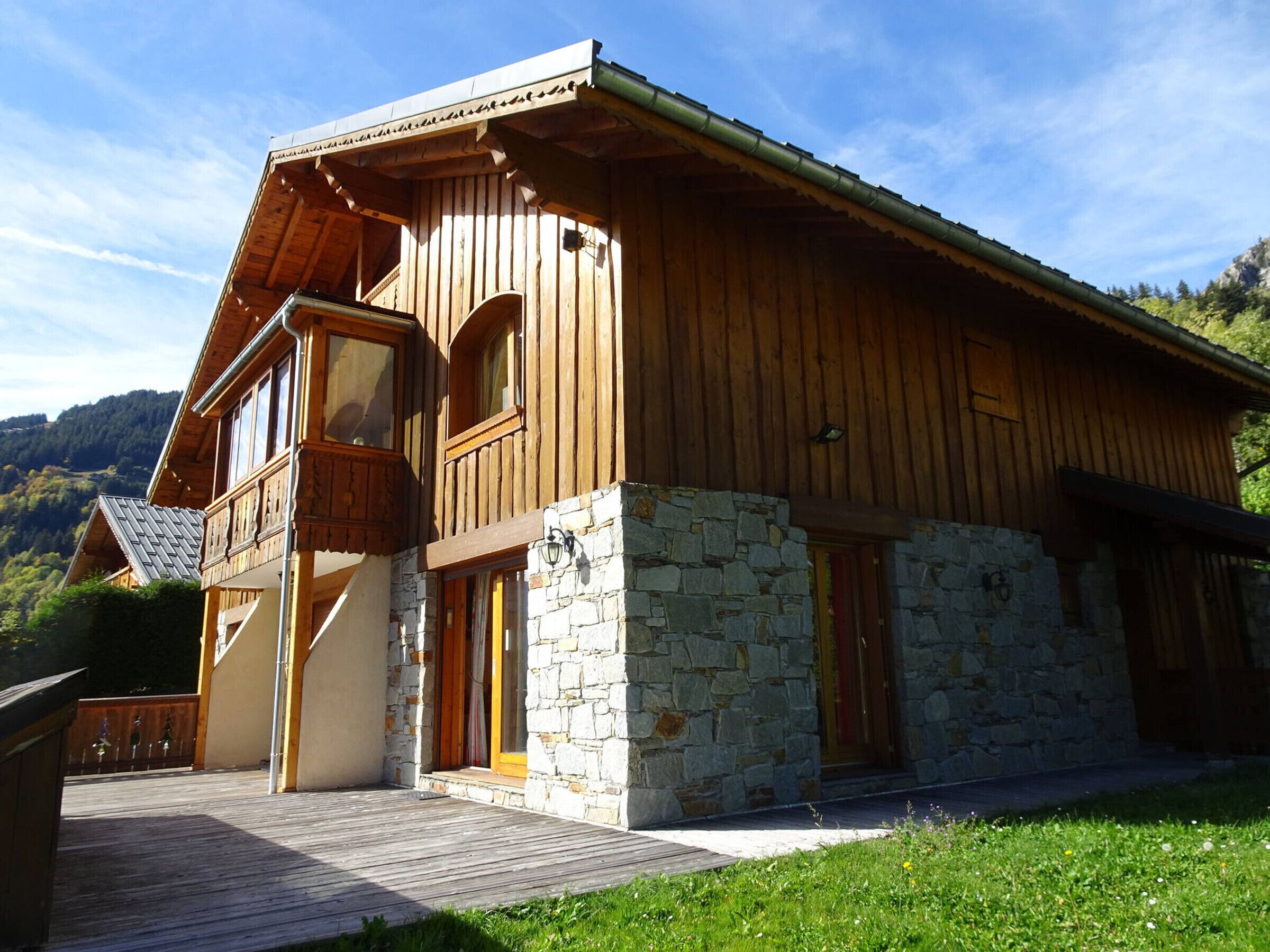 Una cabaña de madera con base de piedra, balcones de madera y una terraza de madera.