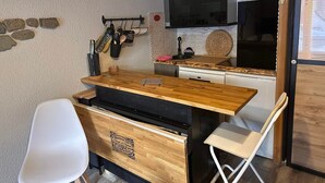 Une cuisine compacte avec un plan de travail en bois, une chaise blanche et un mur en pierres apparentes derrière l’évier.