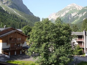 Un edificio in legno con un balcone, circondato da una vegetazione lussureggiante e montagne sullo sfondo.