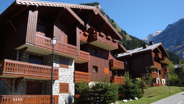 A wooden chalet with balconies, stone foundation, and a mountain backdrop. - 4-room Duplex with balcony and parking in Pralognan, near slopes (Pralognan-la-Vanoise)