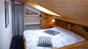 A bedroom with a sloped ceiling, a bed with patterned bedding, a bedside table with a lamp, and a mirror above the bed. - 4-room Duplex with balcony and parking in Pralognan, near slopes (Pralognan-la-Vanoise)