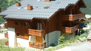 A wooden chalet with a sloped roof, multiple balconies, and a stone foundation. - 4-room Duplex with balcony and parking in Pralognan, near slopes (Pralognan-la-Vanoise)