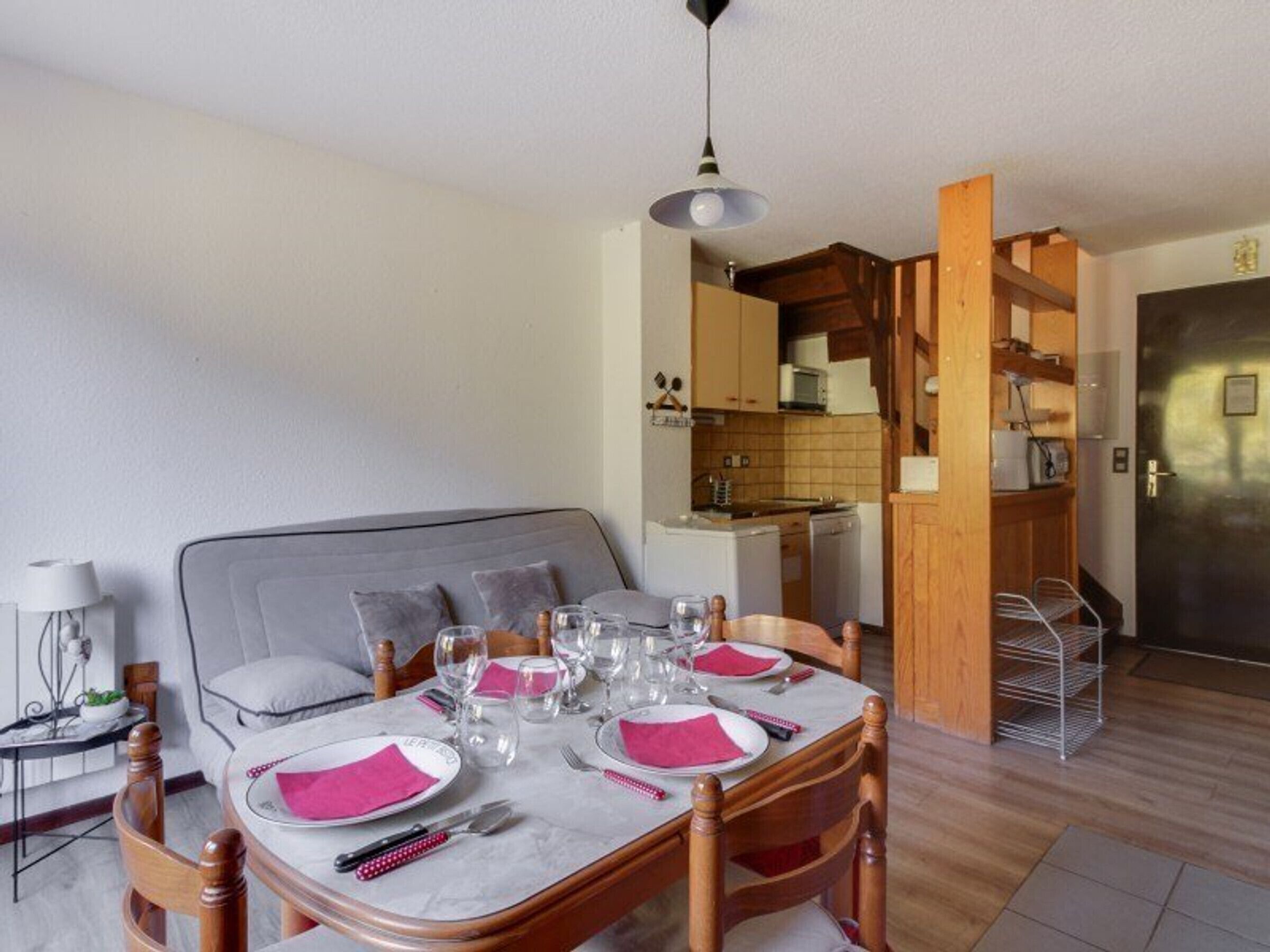 A dining area with a table set for four, a sofa, a lamp, and a kitchen in the background.