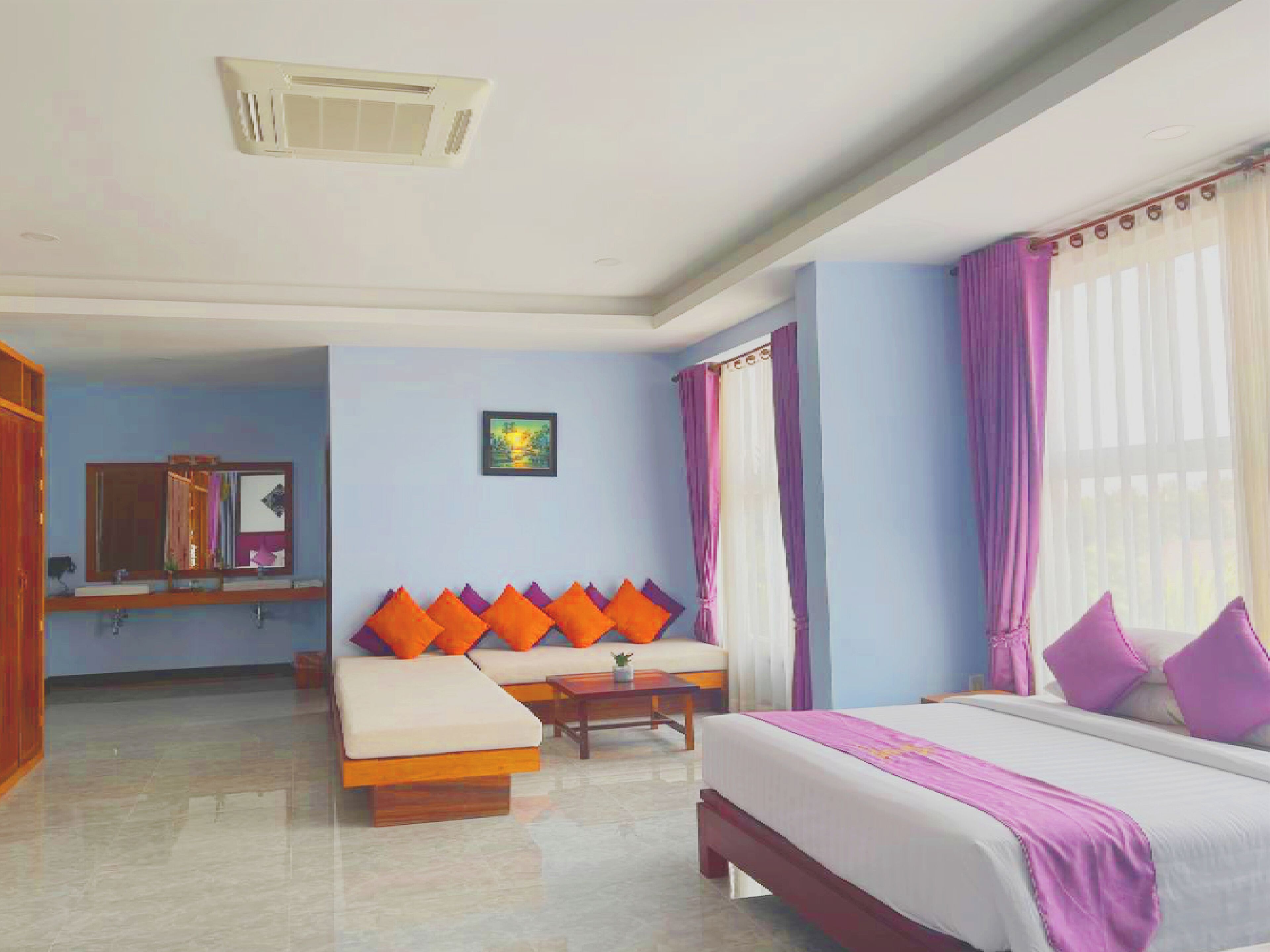 Habitación de hotel con cama, sofá, una mesita, espejo y ventana con cortinas.