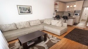 A living room with a sofa, coffee table, and a kitchen area with a microwave and cabinets. - Apartment Rubin (Belgrade)