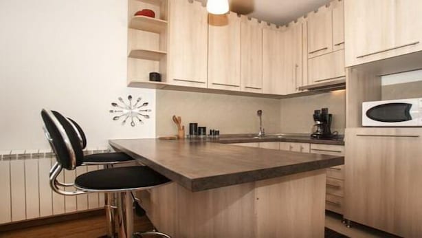 A kitchen with wooden cabinets, a black chair, a microwave, and a coffee maker. - Apartment Rubin (Belgrade)
