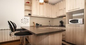 A kitchen with wooden cabinets, a black chair, a microwave, and a coffee maker. - Apartment Rubin (Belgrade)
