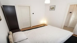 A bedroom with a bed, a nightstand, a door, and a wall-mounted picture. - Apartment Rubin (Belgrade)