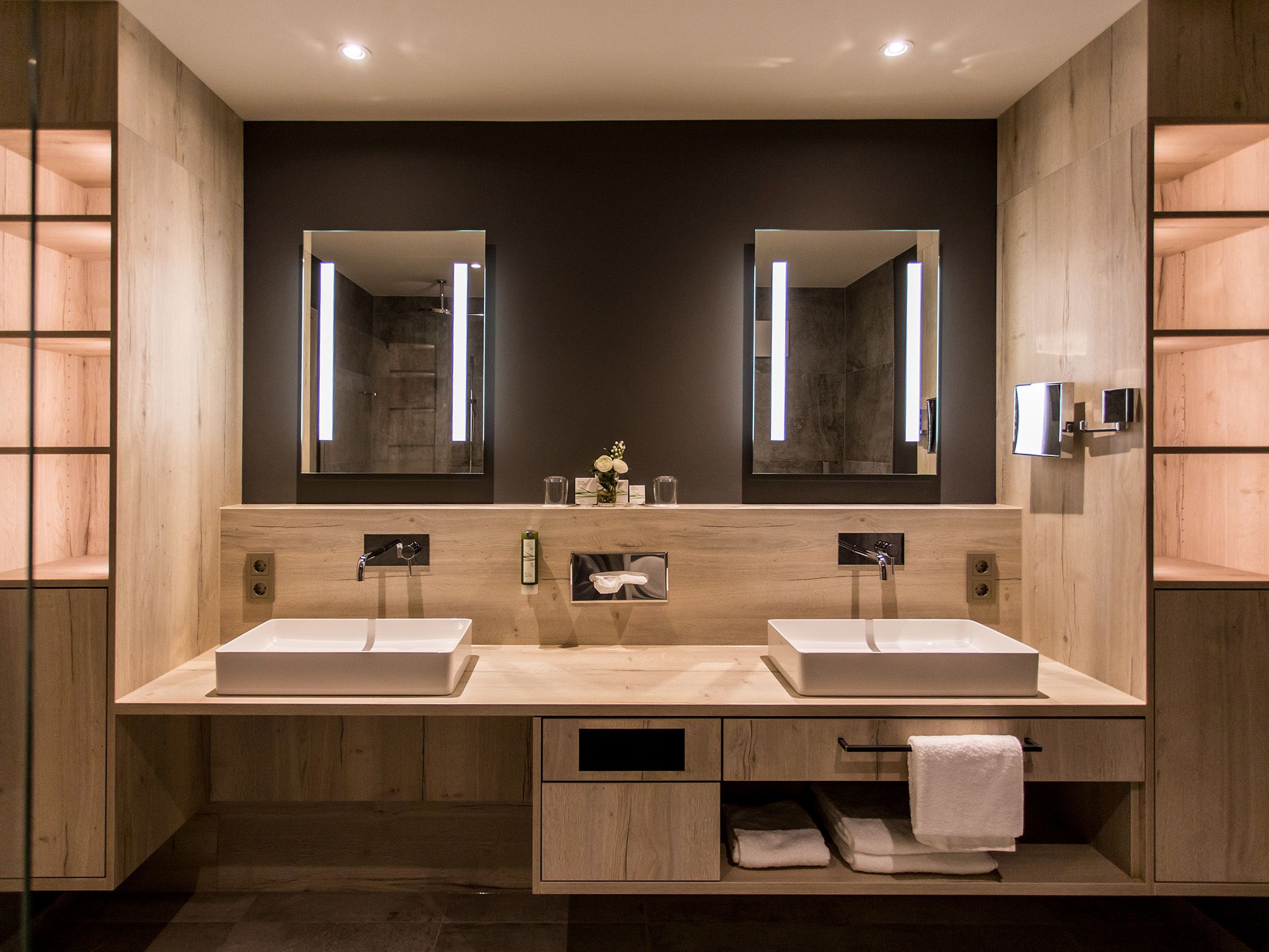 A modern bathroom with two sinks, large mirrors, and wooden cabinetry.