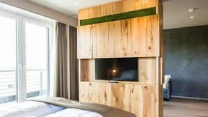 Una habitación de hotel moderna con una cama grande, un televisor montado en una pared de paneles de madera y un balcón con cortinas.