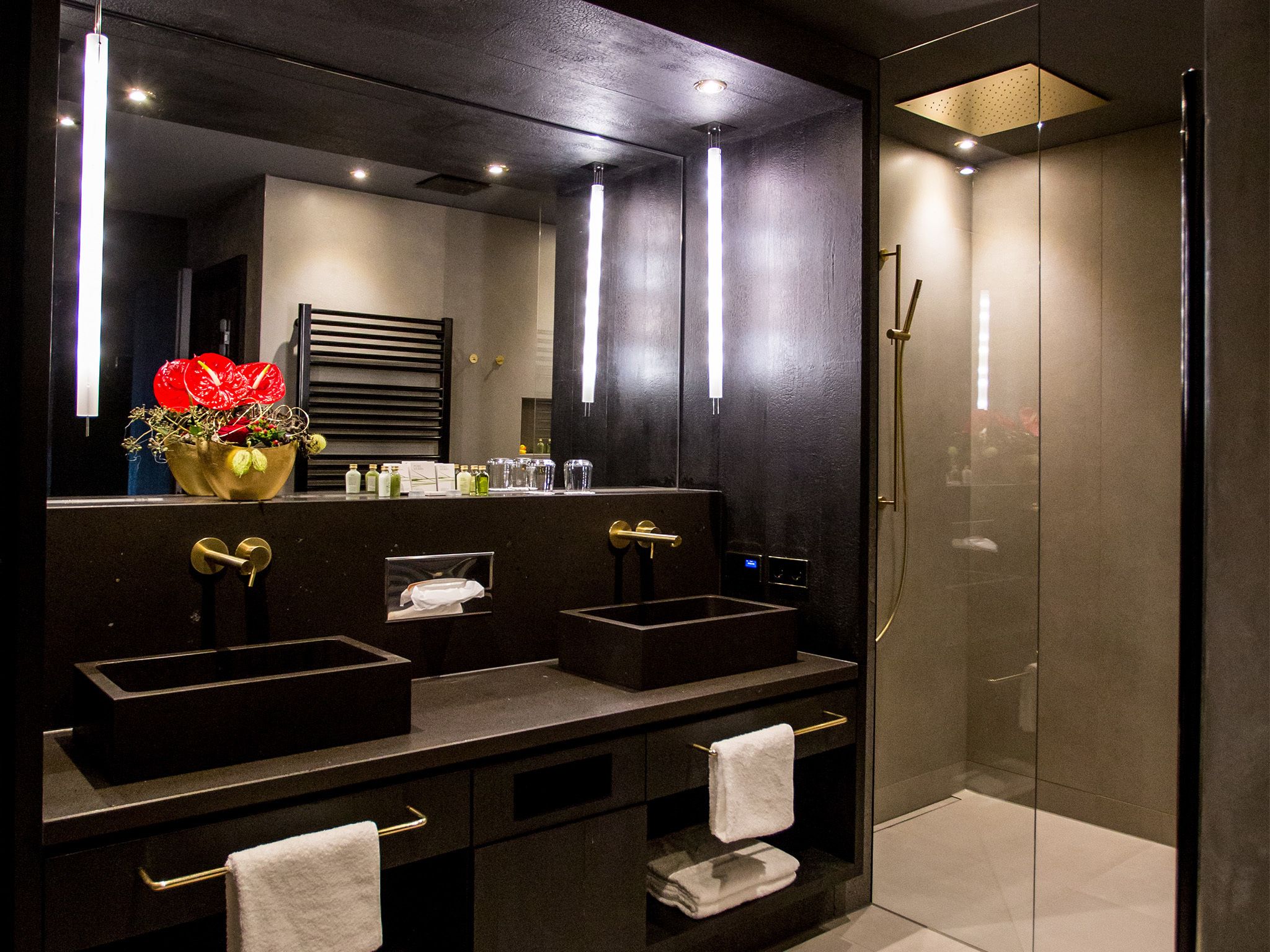 Een moderne badkamer met twee wastafels, een grote spiegel en een douche met glazen wanden.
