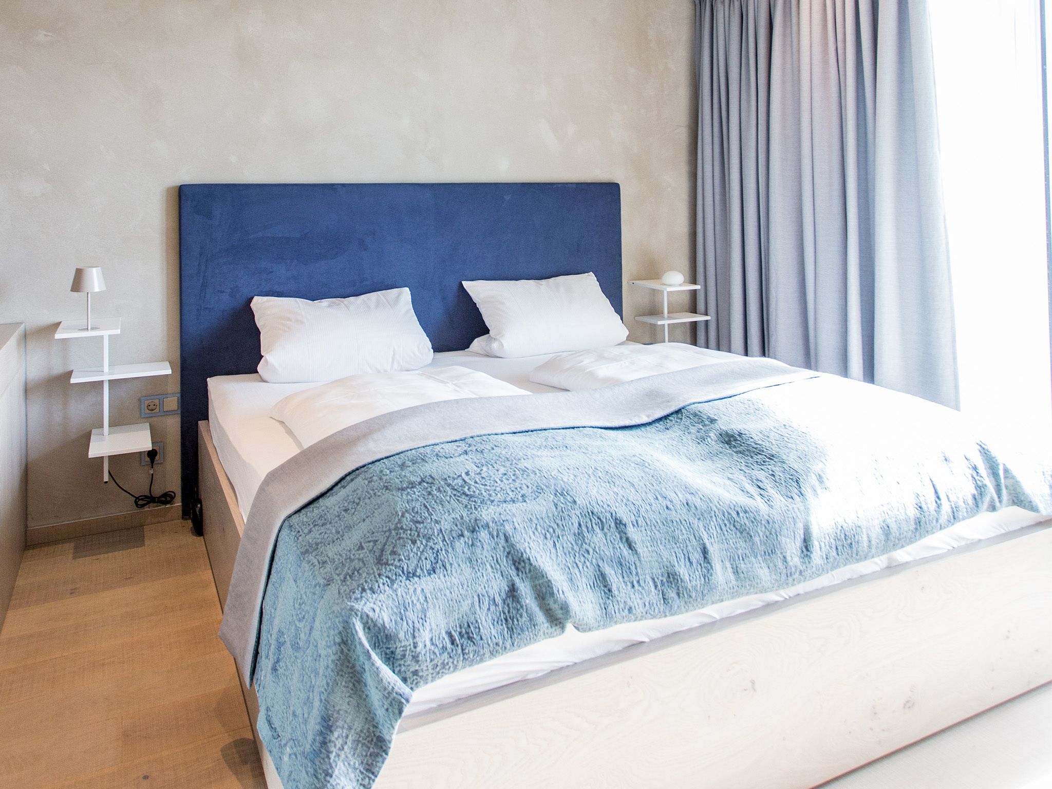 A neatly made bed with a blue headboard, white bedding, and a grey blanket.