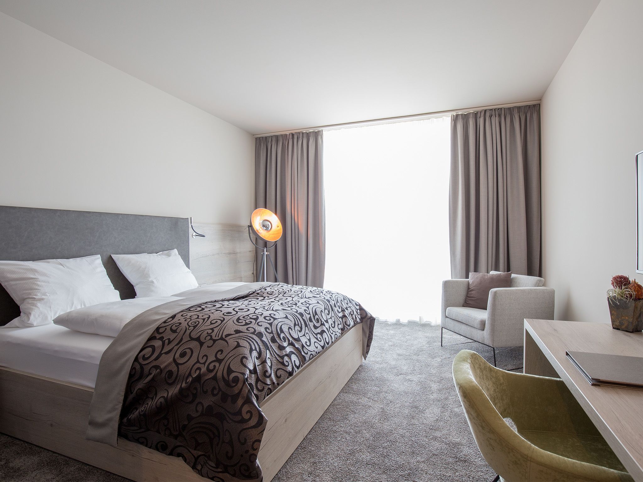 Una habitación de hotel con una cama, un escritorio, una silla y una lámpara.