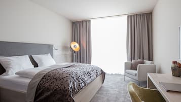 A hotel room with a bed, a desk, a chair, and a lamp.