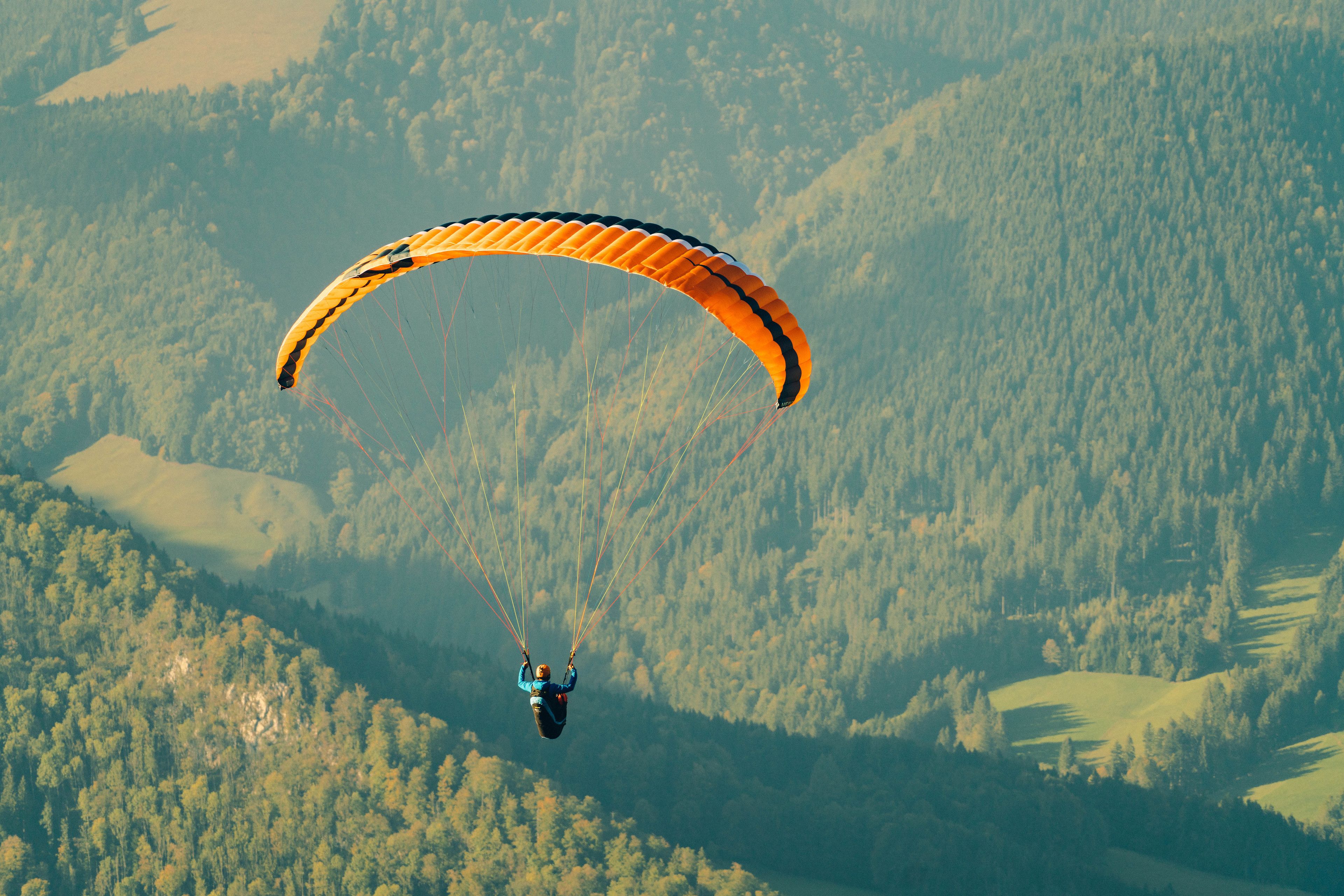 A person paragliding over a forested mountainous area.
