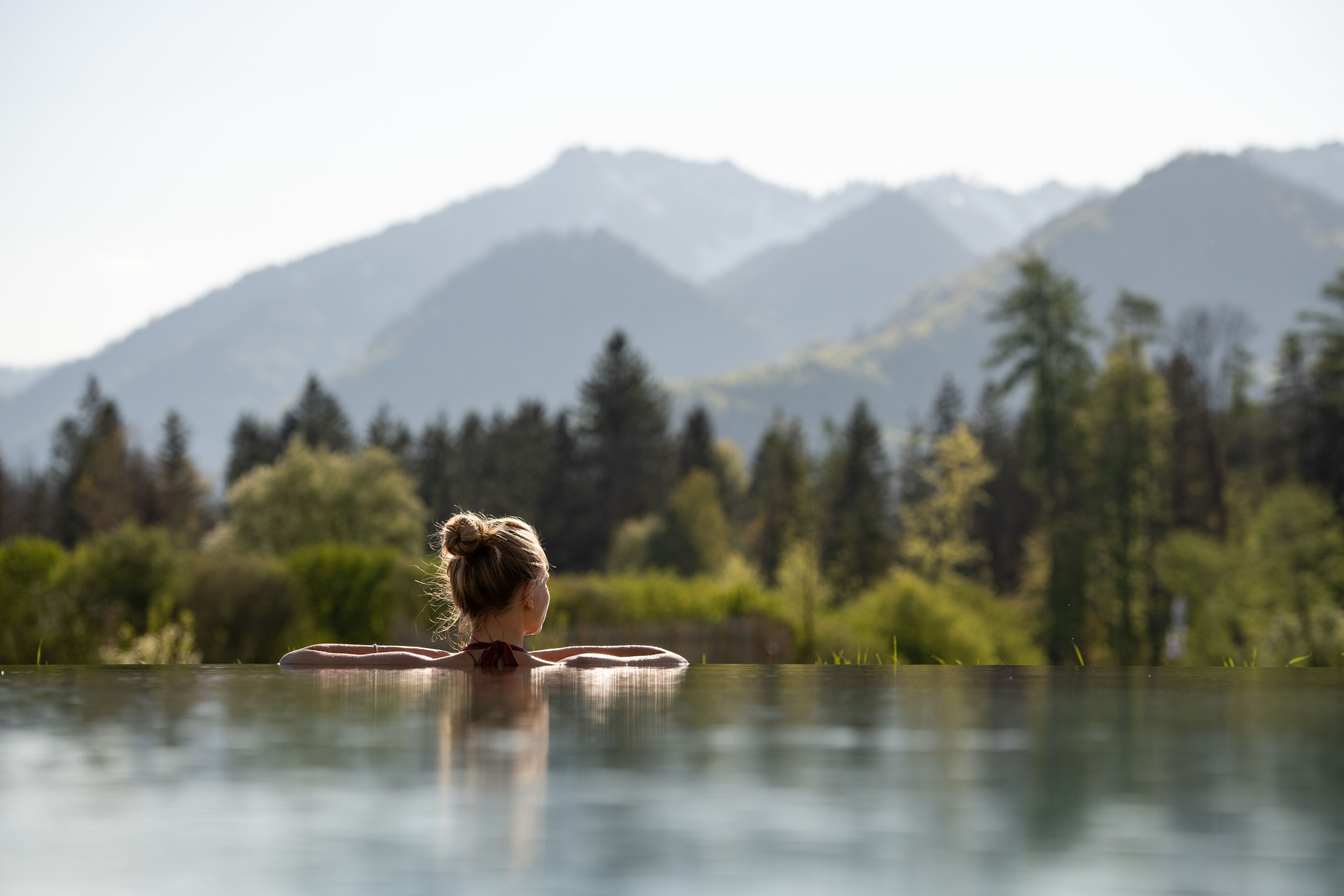 A person relaxing in a clear pool with a mountainous landscape in the background.