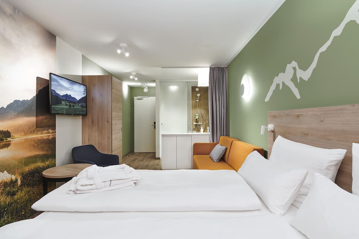 A hotel room with a bed, a TV, a desk, and a view of a mountain landscape.