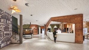 A spacious lobby with a reception desk, a staircase, and a mural on the left wall. - aja Ruhpolding (Ruhpolding)