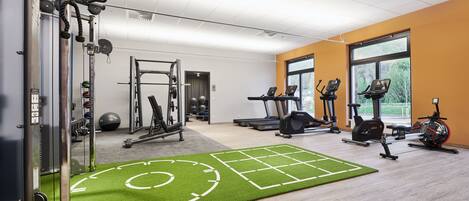 Un gimnasio con equipo de ejercicio variado, una colchoneta de césped artificial y amplias ventanas.