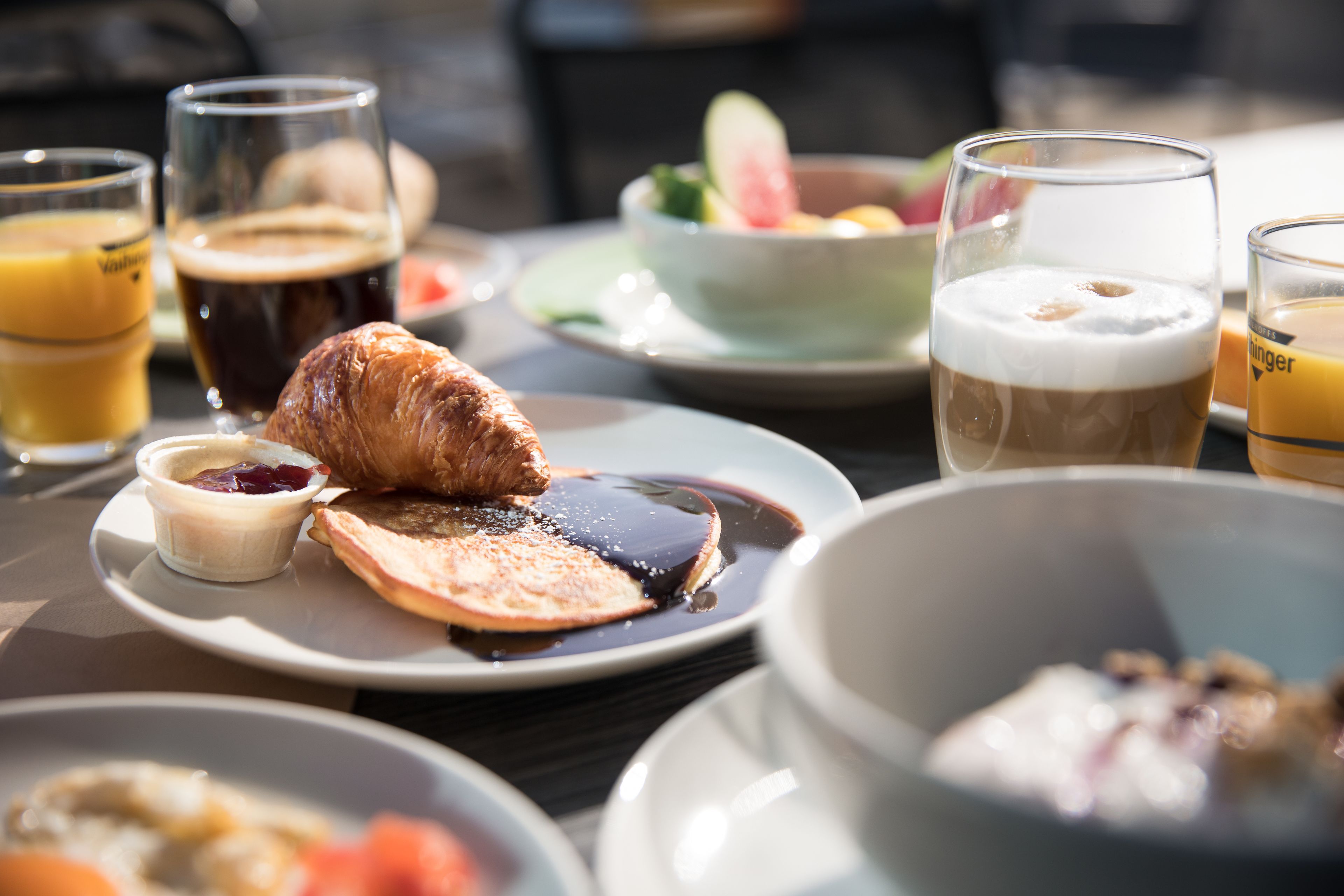 A breakfast setting with various dishes, drinks, and a croissant on a plate.