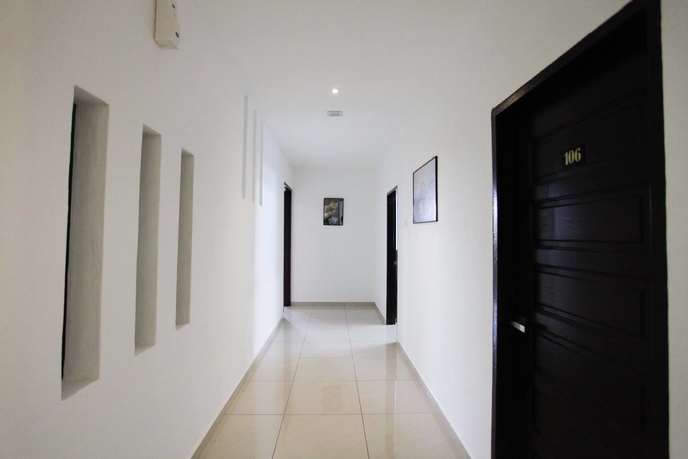 A hallway with white walls, a black door on the right, and a tiled floor.