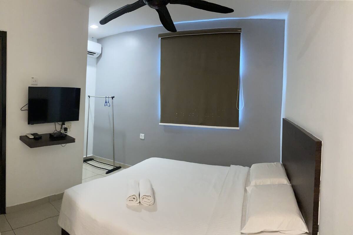 A hotel room with a bed, a TV, a mirror, and a ceiling fan.