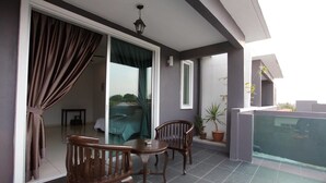 Un balcon avec deux chaises en bois et une petite table, une porte-fenêtre coulissante donnant sur une chambre, et une plante en pot.