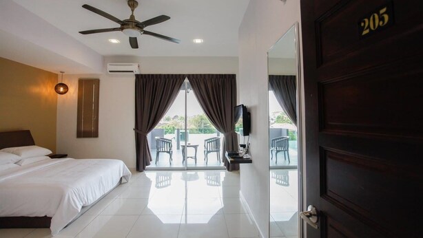 Une chambre d’hôtel avec un lit, un ventilateur de plafond, une télévision et un balcon équipé de chaises.