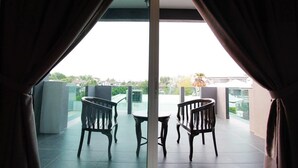 Un balcon avec deux chaises en bois et une petite table, donnant sur un quartier résidentiel avec des maisons et des arbres.