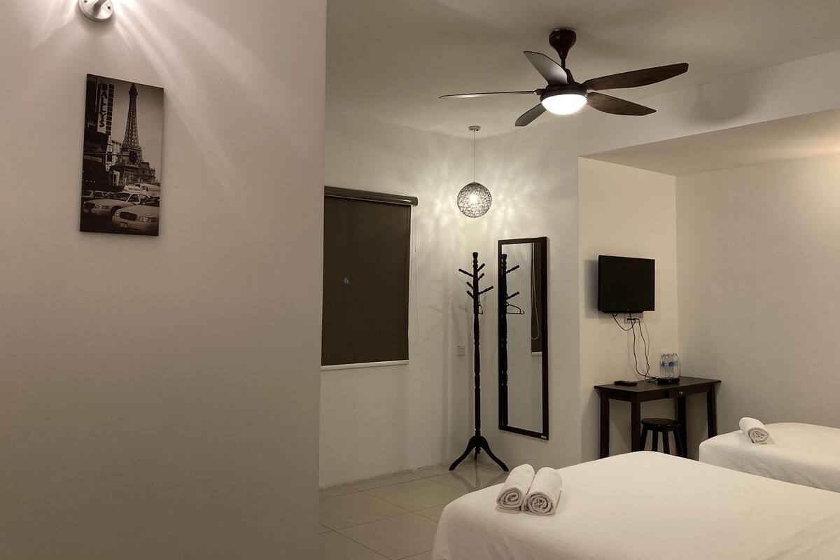 A hotel room with two beds, a ceiling fan, a wall-mounted TV, a mirror, and a picture of the Eiffel Tower.