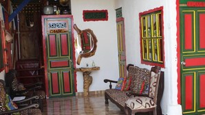 Una habitación con un banco de madera, una silla, una mesita con un espejo y una puerta con paneles de colores.