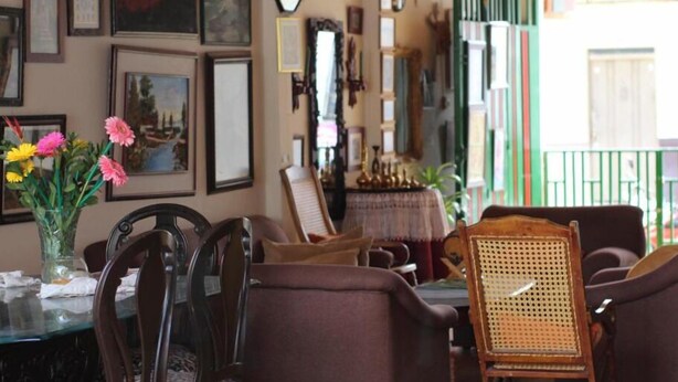 Un comedor con sillas de madera y una mesa, fotografías enmarcadas en la pared y un jarrón con flores.