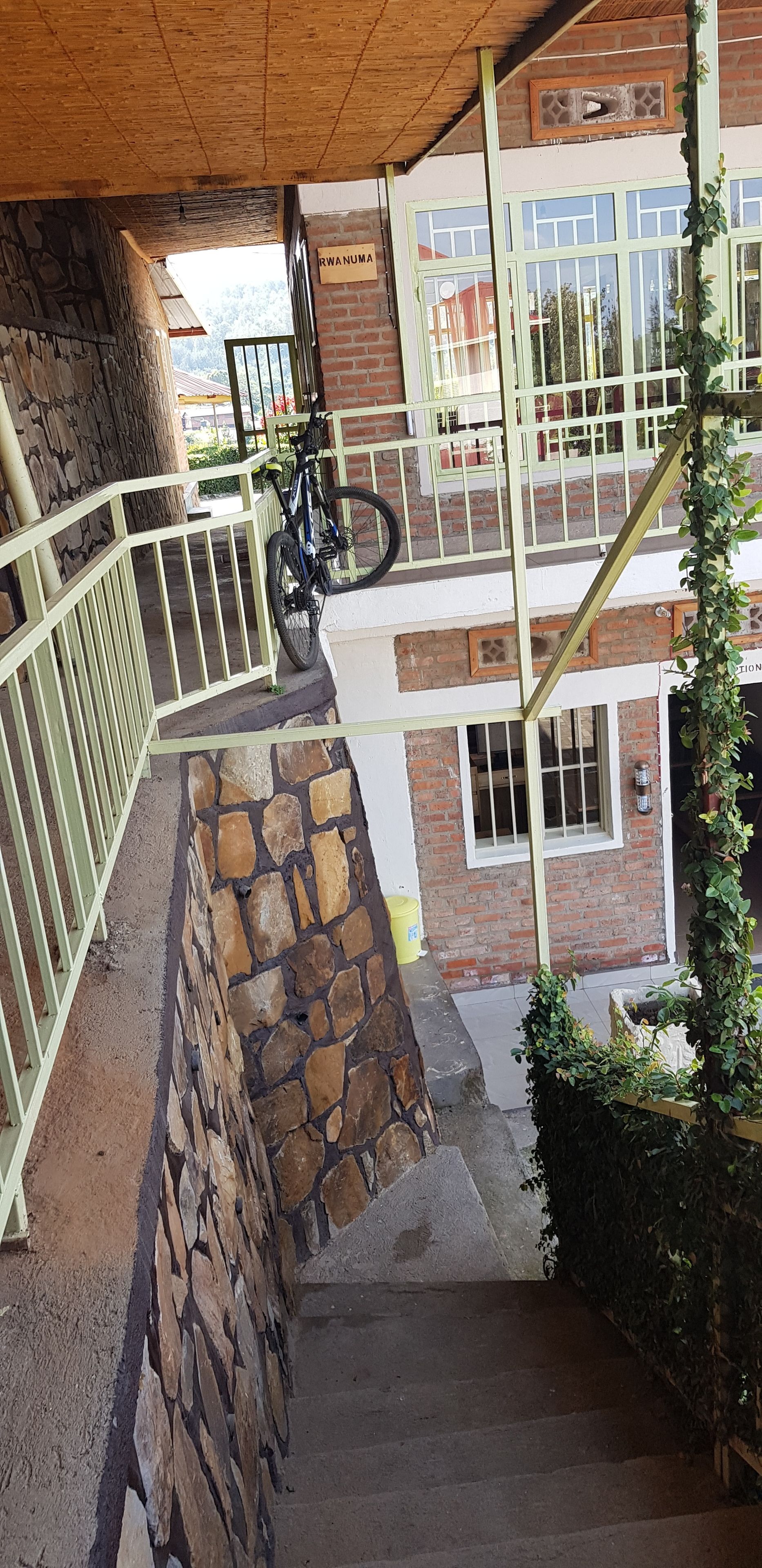 Un edificio de varios niveles con una pared de piedra, una bicicleta y un letrero que dice "RWANUMA".