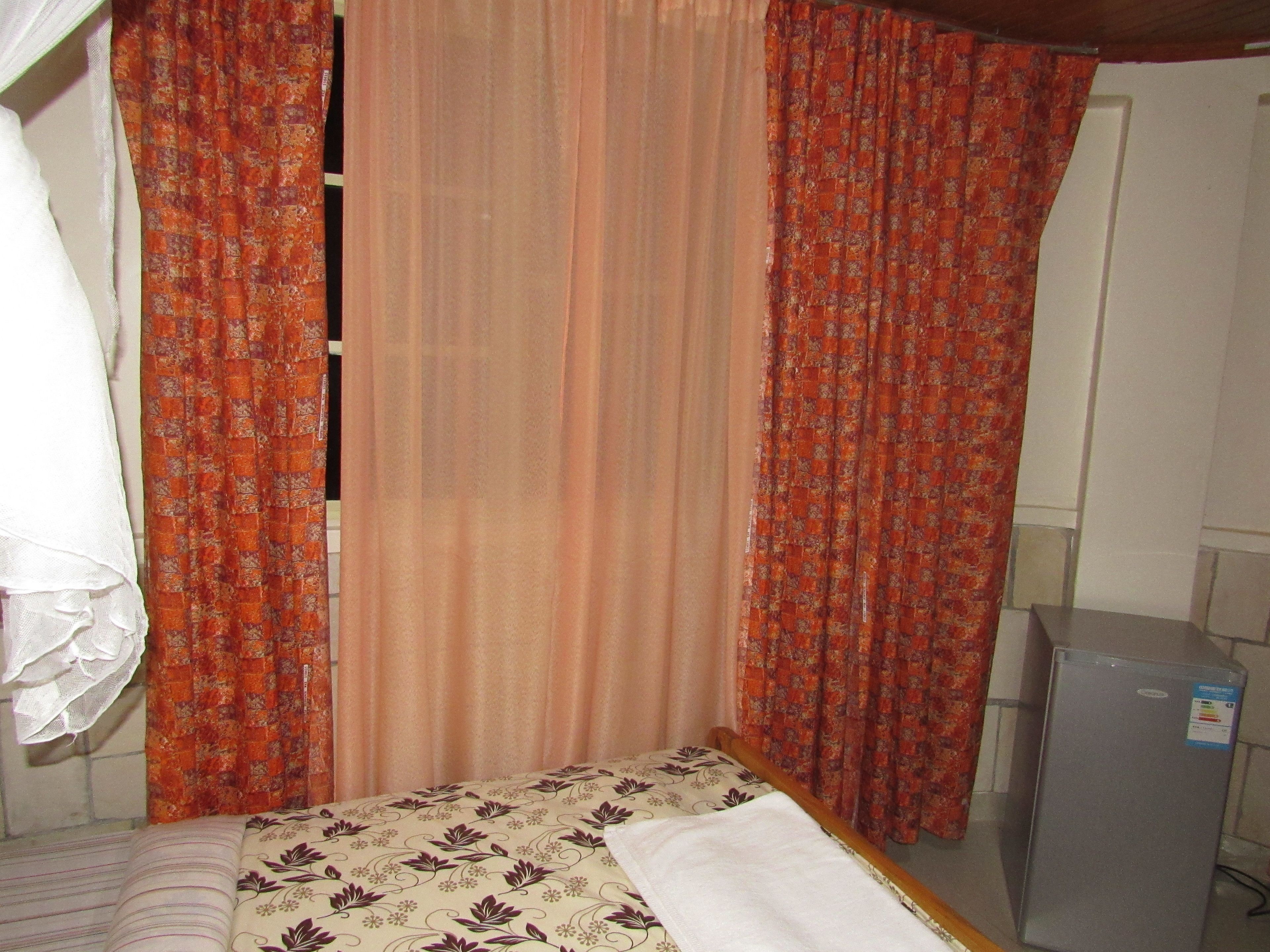 A small, single-bed room with a bed, a nightstand, a refrigerator, and curtains.