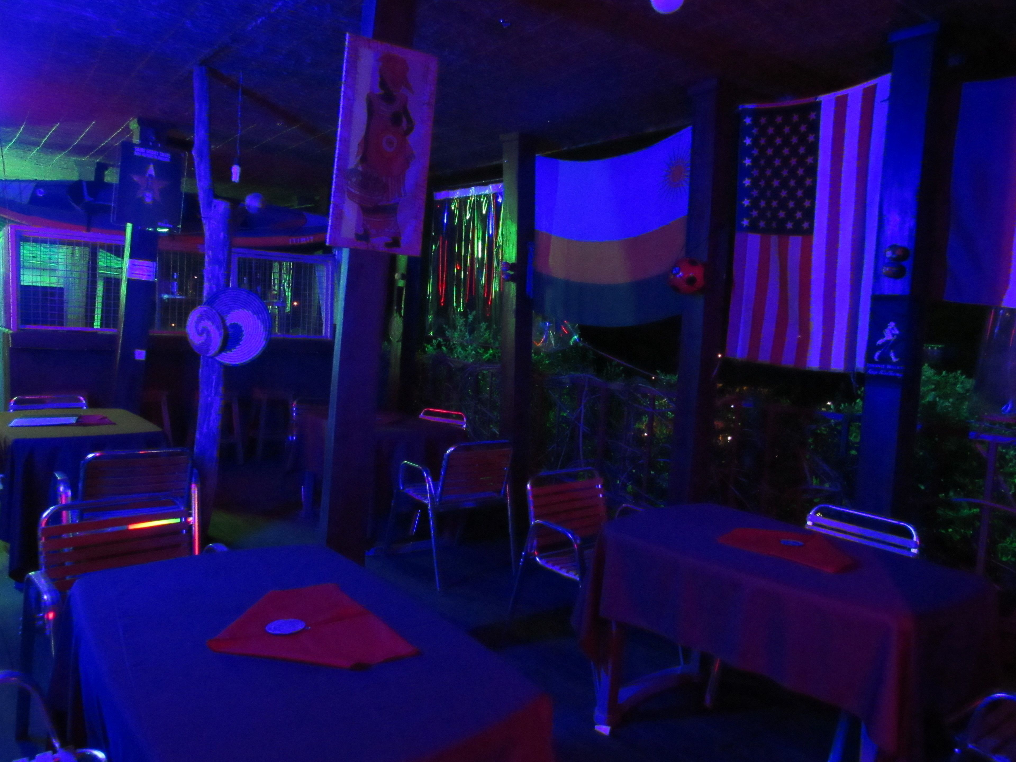 A dimly lit restaurant with tables and chairs, an American flag, and a flag of another country.