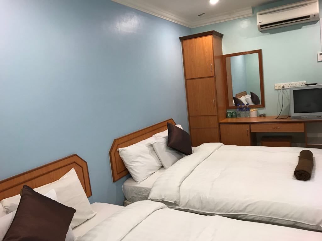 A hotel room with two beds, a wooden wardrobe, a desk with a computer, and a mirror.