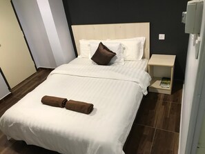 A neatly made bed with white linens and two brown towels, a wooden headboard, and a small bedside table with a book. - Seri Kangsar KK Hotel (Kuala Kangsar)