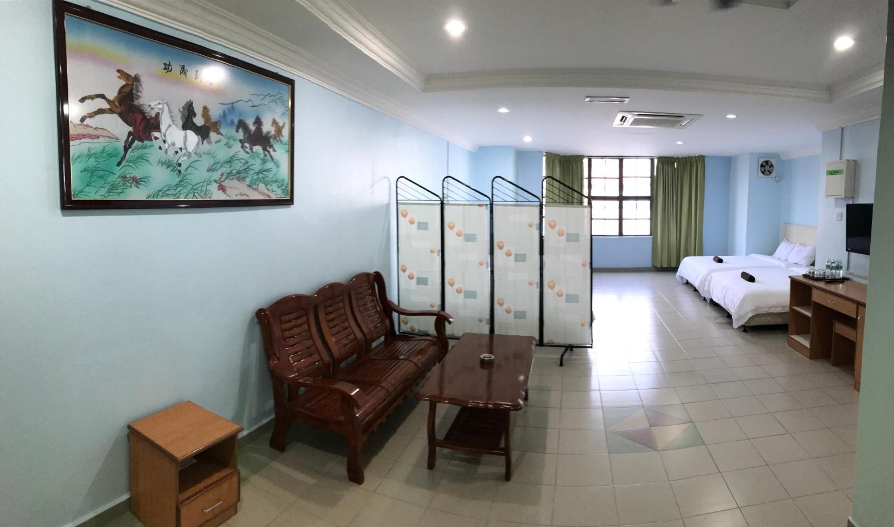 A hotel room with a wooden sofa, a small table, a TV, a bed, and a window with curtains.